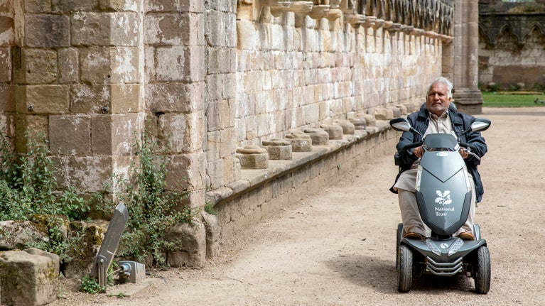 Older man using National Trust mobility scooter to explore the ancient abbey ruins on a summers day